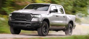 A silver 2026 Ram 1500 drives along a back country road kicking up dirt. New 2026 Ram 1500 for sale at Blenheim Chrysler Dodge Jeep Ram. Return of the HEMI V8.